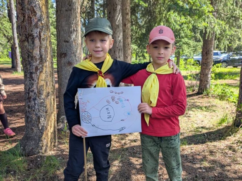 Двоє наймолодших пластунів тримають саморобний плакат у лісі